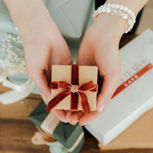 deux mains présentant un petit cadeau avec ruban rouge