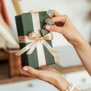 Mains montrant un paquet cadeau vert ruban doré